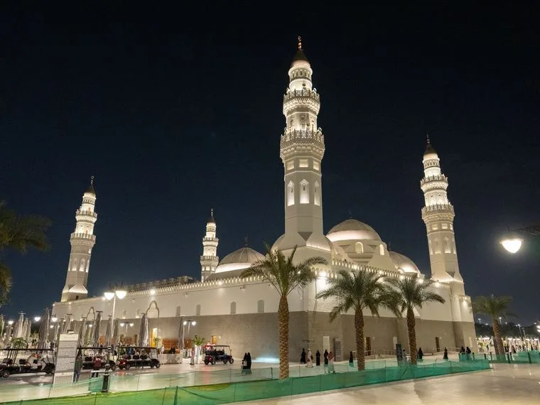 Masjid Quba in Madinah, 's avonds verlicht, met palmbomen ervoor