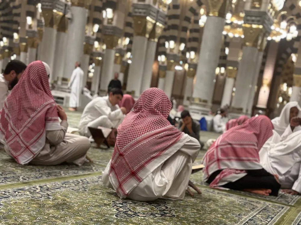 Een Qur'an-kring tussen de zuilen van Masjid an-Nabawi: mannen zitten met de mushaf op het groene tapijt